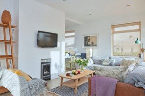 Ein modernes Wohnzimmer mit Fernseher, Sofa, Couchtisch und Kamin.