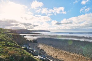 Eine Küstenlandschaft mit Kiesstrand, grasbewachsenen Klippen und blauem Himmel.
