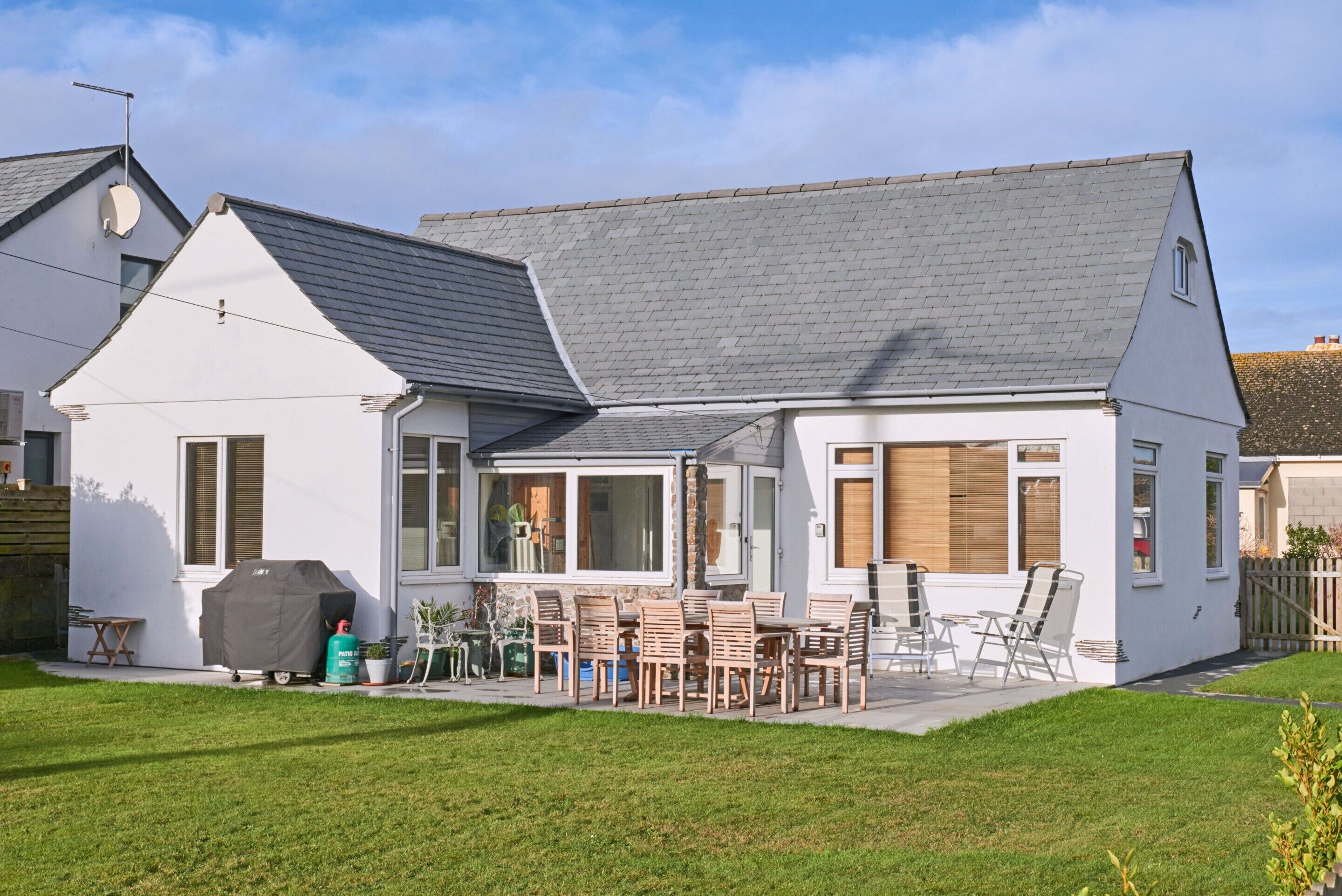 A two-story house with a patio area, outdoor furniture, and a barbecue grill.