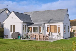 Ein zweistöckiges Haus mit Terrasse, Gartenmöbeln und Grill.