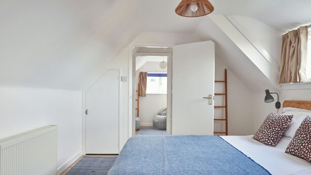 Une chambre à coucher avec un lit, un radiateur, une porte, une fenêtre et un luminaire suspendu.
