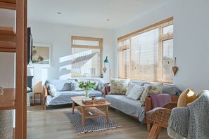 Ein Wohnzimmer mit einer Couch, einem Couchtisch mit Büchern und einem Fenster mit Jalousien.