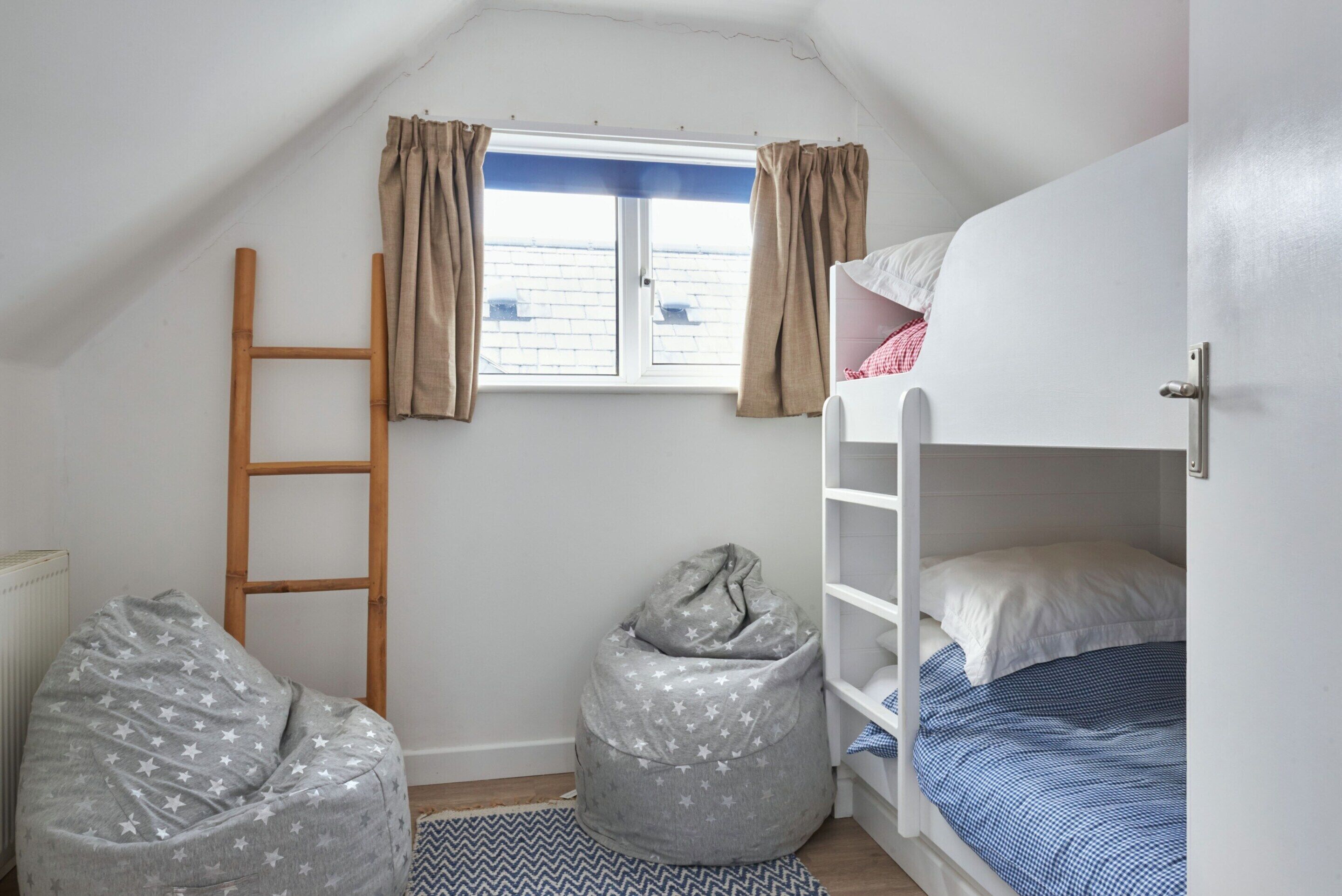 A child's bedroom with bunk beds, a ladder, and two bean bags.