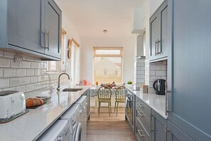 A modern kitchen with grey cabinets, a stainless steel sink, and a built-in washing machine. - Coastal Family House for 8 in Cornwall (Bude)