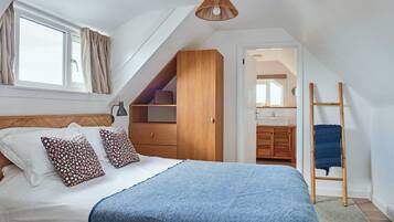 A bedroom with a bed, a wooden wardrobe, a hanging light fixture, and a view into an adjacent bathroom.