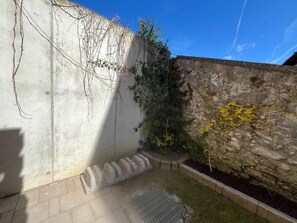 Ein Innenhof mit einer Steinmauer, einer Betonmauer mit Weinreben und einem Metallgitter auf dem Boden.