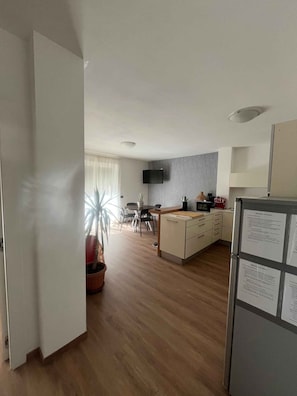 A modern kitchen with a dining area, a flat-screen TV mounted on the wall, and a refrigerator with papers attached. - Holiday apartment - a home-from-home in the Ledro Valley – Modern & Cosy (Tiarno Di Sopra)