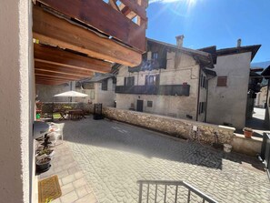 Un espace extérieur aménagé en terrasse, avec un sol en pierre, des poutres en bois au-dessus et une table entourée de chaises.
