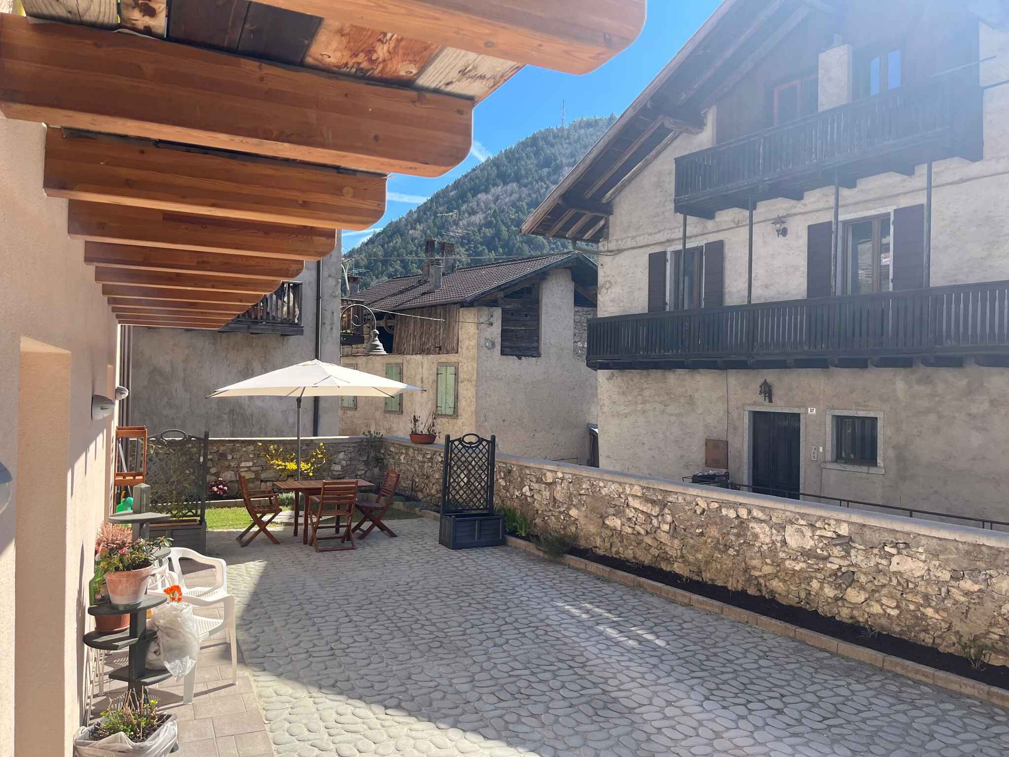 En gårdhave med et bord, stole, en træpergola og en stenvæg.