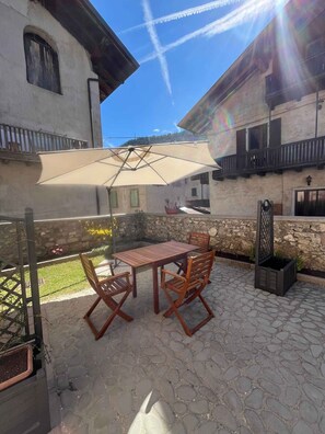Eine Terrasse im Freien mit Tisch und Stühlen, einem großen Sonnenschirm und einer Steinmauer.