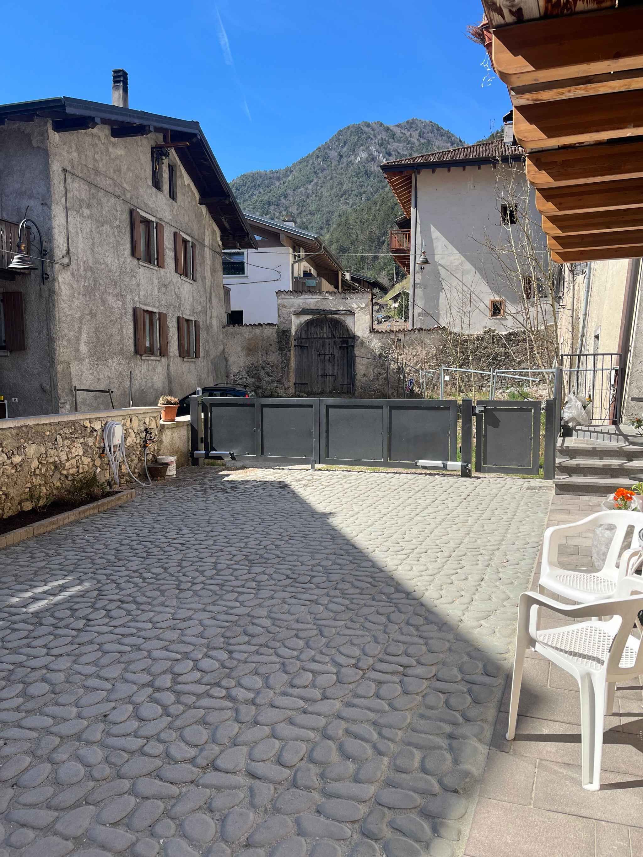 En innergård med kullerstenar, en grind av metall och en byggnad med en mur av sten.