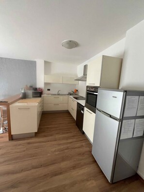A compact kitchen with white cabinets, a built-in oven, and a refrigerator. - Holiday apartment - a home-from-home in the Ledro Valley – Modern & Cosy (Tiarno Di Sopra)