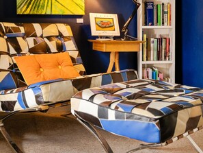 Ein modernes Wohnzimmer mit einer Couch, einem Hocker, einem Bücherregal und einem gerahmten Bild auf einem kleinen Tisch.
