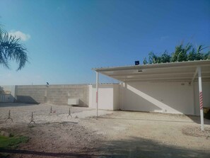 Ein Gebäude mit flachem Dach und überdachtem Bereich, umgeben von einer Betonmauer und sandigem Untergrund.