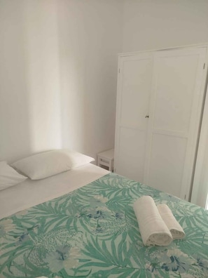 Ein Zimmer mit einem Bett, einem weißen Kleiderschrank und einem kleinen Nachttisch.