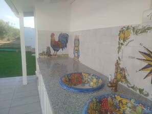 A kitchen with a tiled backsplash featuring colorful artwork, a granite countertop, and a sink with a faucet. - Villa with garden and air conditioning (Santa Maria del Focallo)