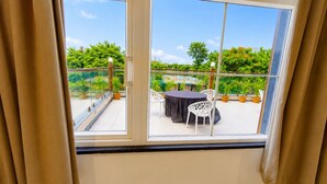 A balcony with a table and chairs, potted plants, and a clear view of greenery. - Hotel Mewada (Ujjain)