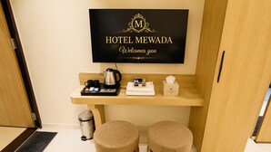 Habitación de hotel con una televisión mostrando el nombre del hotel, una mesita con un atrezo de cortesía, dos pufs y un cubo de basura.
