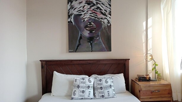 Een slaapkamer met een bed, een hoofdbord, een nachtkastje en een schilderij aan de muur.