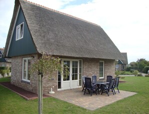 A house with a thatched roof, a brick exterior, and a patio with outdoor furniture. - Detached Spacious Beach Villa for 8 (Makkum)