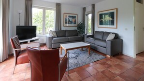 Ein Wohnzimmer mit Fernseher, zwei Sofas, einem Couchtisch und einem Essbereich mit Stühlen.