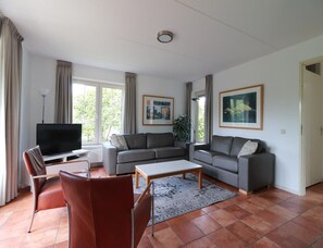 A living room with a TV, two sofas, a coffee table, and a dining area with chairs. - Detached Spacious Beach Villa for 8 (Makkum)
