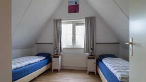 Ein schräges Schlafzimmer im Dachgeschoss mit zwei Betten, einem Fenster mit Vorhängen und einer Heizung.