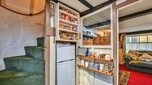 Una cucina compatta con frigorifero, scaffali pieni di oggetti, una scala e un soggiorno con divano e tappeto.