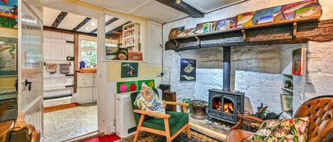 Una habitación acogedora con chimenea, una silla de madera, una alfombra roja y una estantería llena de libros y objetos decorativos.
