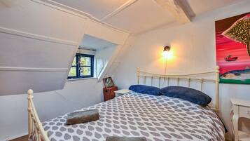 A bedroom with a sloped ceiling, a bed with patterned bedding, a nightstand, a wall-mounted light, and a window with a view of a boat.