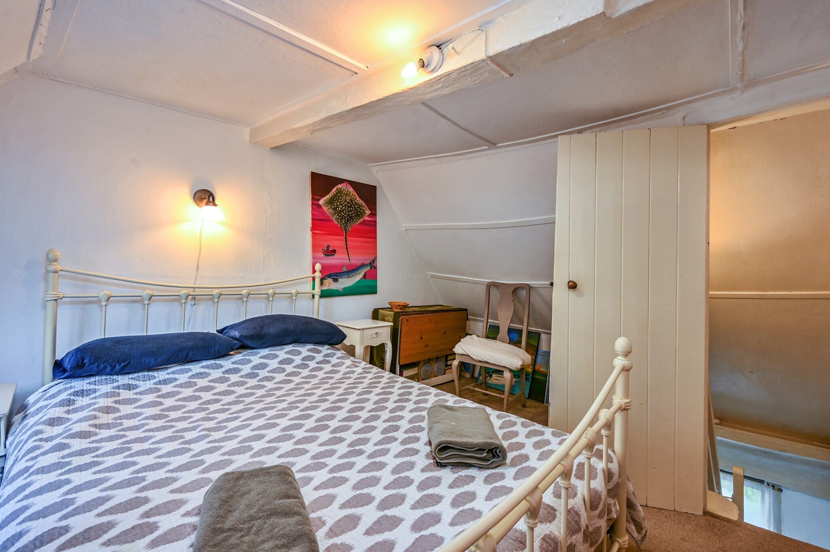 A bedroom with a bed, a nightstand, a chair, a painting, and a door.