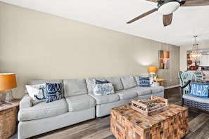 A living room with a striped sofa, a wooden coffee table, and a ceiling fan. - Emerald Isle Unit 1402 (Pensacola Beach)