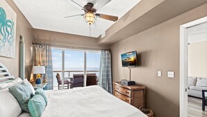 Quarto com cama, televisão, ventoinha no teto e vista para o mar.