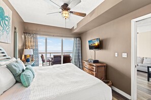 A bedroom with a bed, a television, a ceiling fan, and a view of the ocean. - Emerald Isle Unit 1402 (Pensacola Beach)