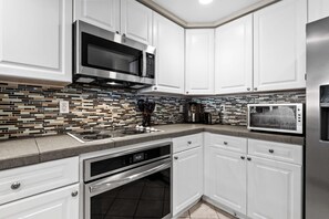 A modern kitchen with white cabinets, stainless steel appliances, and a mosaic tile backsplash. - Emerald Isle Unit 1402 (Pensacola Beach)
