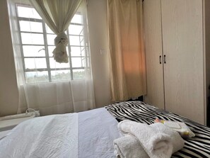 Ein Schlafzimmer mit einem Bett, einem Fenster mit Vorhängen, einem Kleiderschrank und einem Kissen mit ZEBRA-Muster.