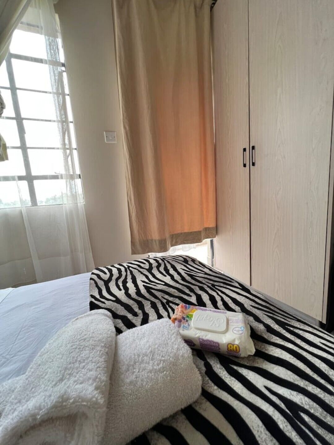 A bedroom with a zebra-patterned bedspread, a white towel, and a toothbrush on the bed.
