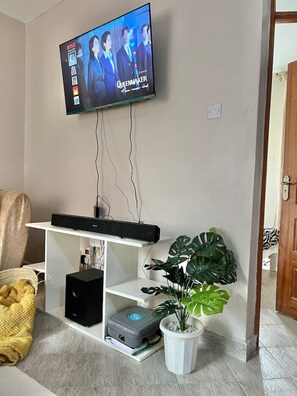 Ein Wohnzimmer mit flachbildfernseher an der Wand, einer weißen Unterhaltungseinheit darunter und einer Blumentopf auf dem Boden.