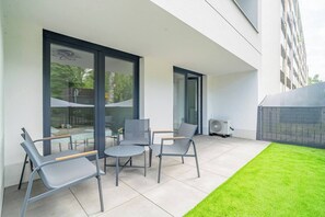 Ein moderner Außenbereich mit Stühlen, einem Tisch, einer kleinen Rasenfläche und einem Gebäude mit großen Fenstern und einem Balkon.