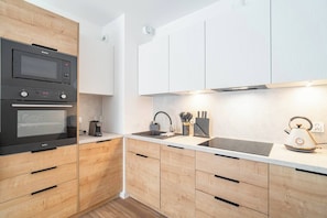 A modern kitchen with wooden cabinets, a built-in oven, a microwave, a kettle, and a sink. - Kraków City Apartment — Terrace & Parking (Kraków)