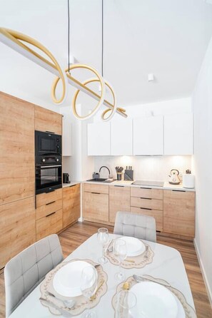 Une cuisine moderne avec des meubles en bois, un four encastré et un coin repas avec une table blanche dressée pour quatre personnes.