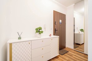Hotellihuone, jossa on valkoinen peilipöytä, puinen ovi, pieni ruukkukasvi ja peili, joka heijastaa huonetta.