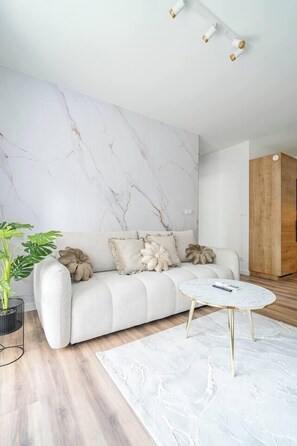 A modern living room with a marble-patterned wall, a light-colored sofa with decorative pillows, a round coffee table, and a wooden cabinet. - Kraków City Apartment — Terrace & Parking (Kraków)