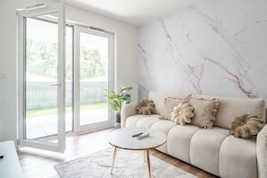 A living room with a sofa, a round coffee table, and a large window with a view of a green lawn. - Kraków City Apartment — Terrace & Parking (Kraków)