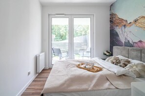 A bedroom with a bed, a bedside table, a radiator, and a view of the outside. - Kraków City Apartment — Terrace & Parking (Kraków)