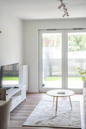 A modern living room with a television, a white radiator, a round coffee table, and a sofa. - Kraków City Apartment — Terrace & Parking (Kraków)
