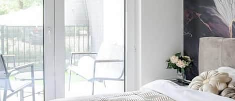 A bedroom with a bed, a tray with cups and a towel, a painting on the wall, and a view of the outdoors through a sliding door.