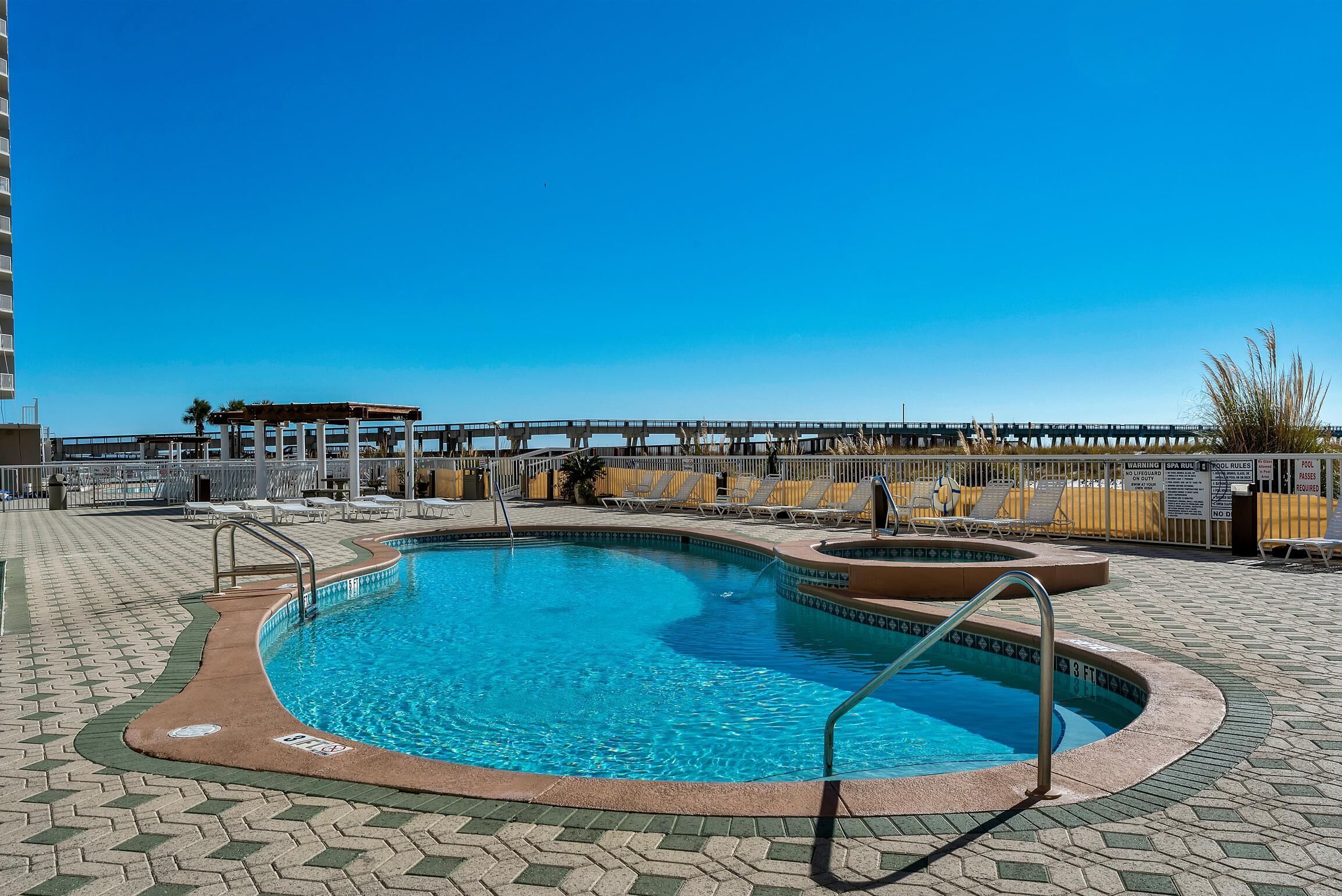 A swimming pool with a sun deck, lounge chairs, and a covered area.