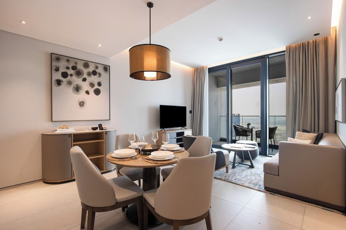 A modern living room with a dining area, a flat-screen TV, and a large window with curtains.