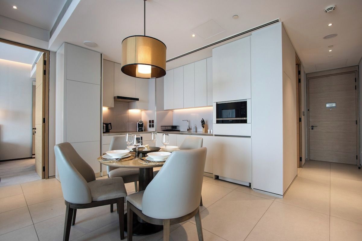 A modern kitchen with white cabinetry, a dining table with chairs, and a pendant light.